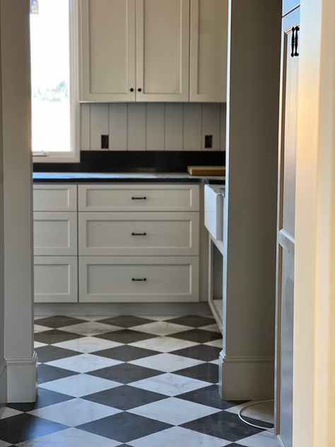 Modern kitchen with white cabinetry, black hardware, and a bold black-and-white checkered marble tile floor.