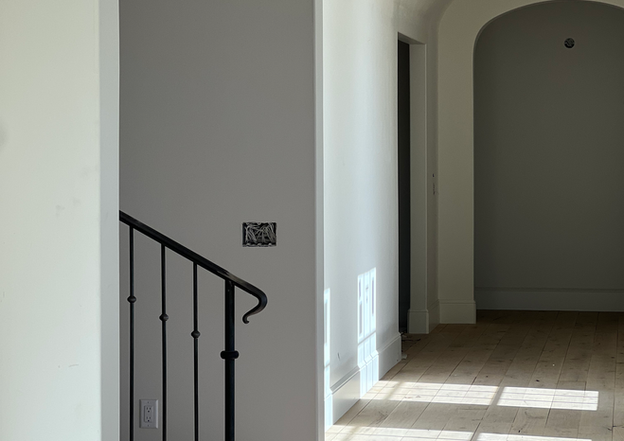 Hallway with light wood floors leading through smooth white arched entryways next to a black metal stair railing.