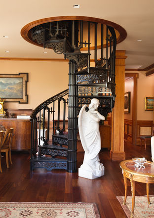 Grand dark wood spiral staircase with a white marble statue at the base in a warm, traditional room.