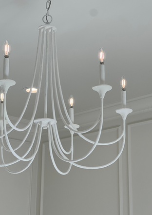 Minimalist white curved chandelier with slender arms and candle-style bulbs against a light gray paneled wall.