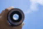 A picture of fingers holding a camera lense looking at clouds.