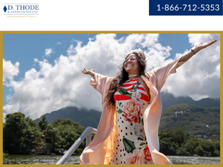 Woman standing on a boat with her arms up in the air smiling with mountains and forests in the background.