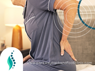 Older woman sitting on her bed in her pajamas, holding her lower back due to pain when she is sick.