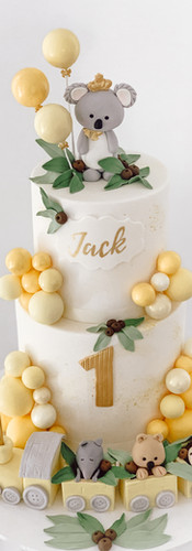 Hand crafted fondant koala atop a 2 teir cake complete with yellow balloons and train set