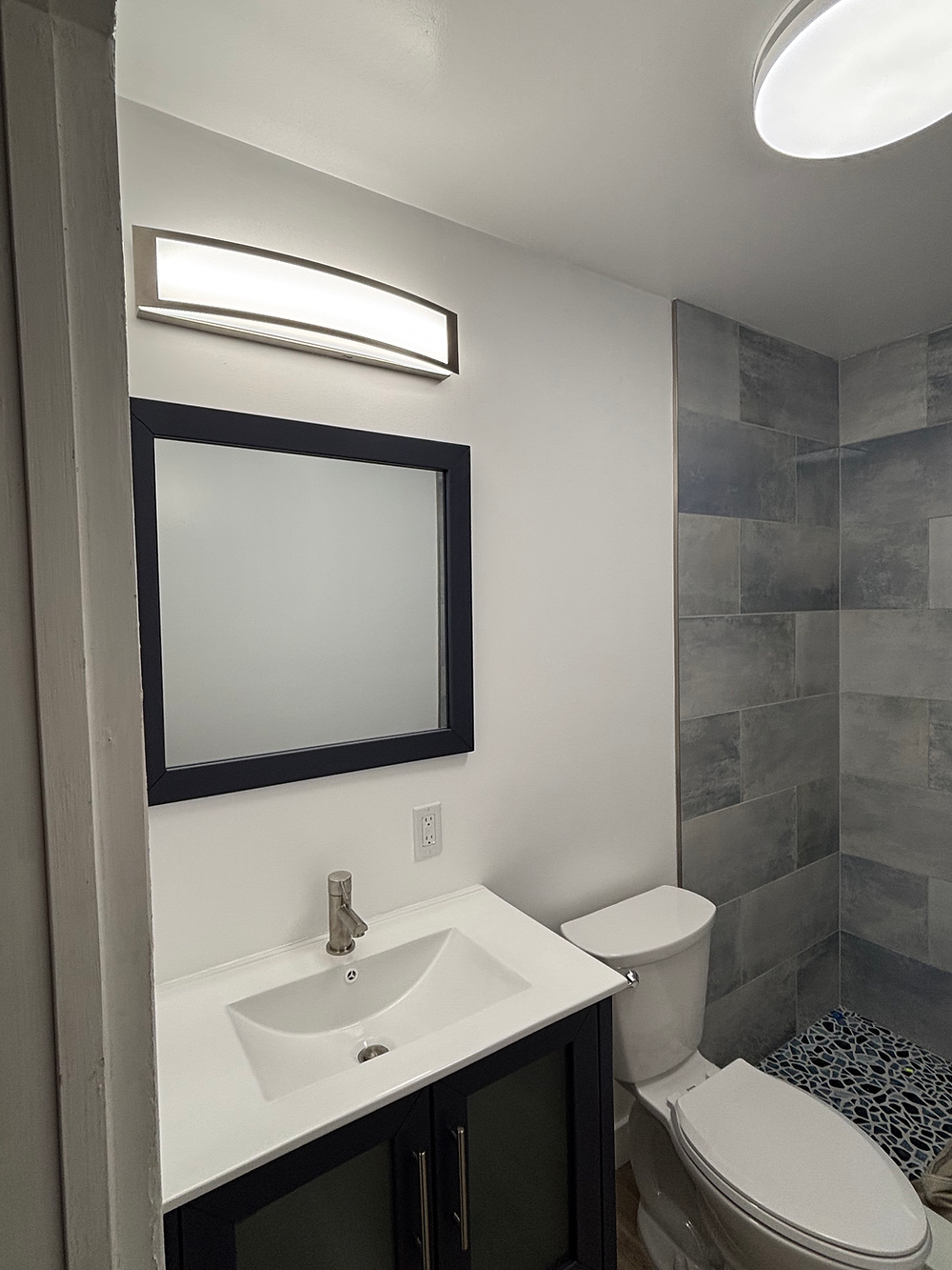Modern bathroom with dark vanity, mirror, toilet, and tiled shower