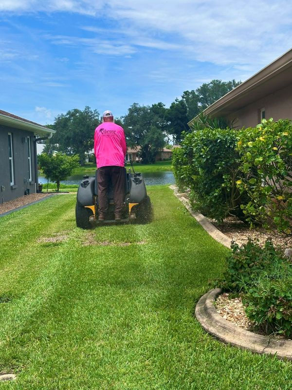 Vibrant Lawn Care worker mowing a residential lawn in North Port with a stand-on mower.