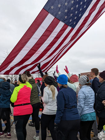 A crowd of people holding a large American flag outdoors, possibly during a parade or patriotic event.