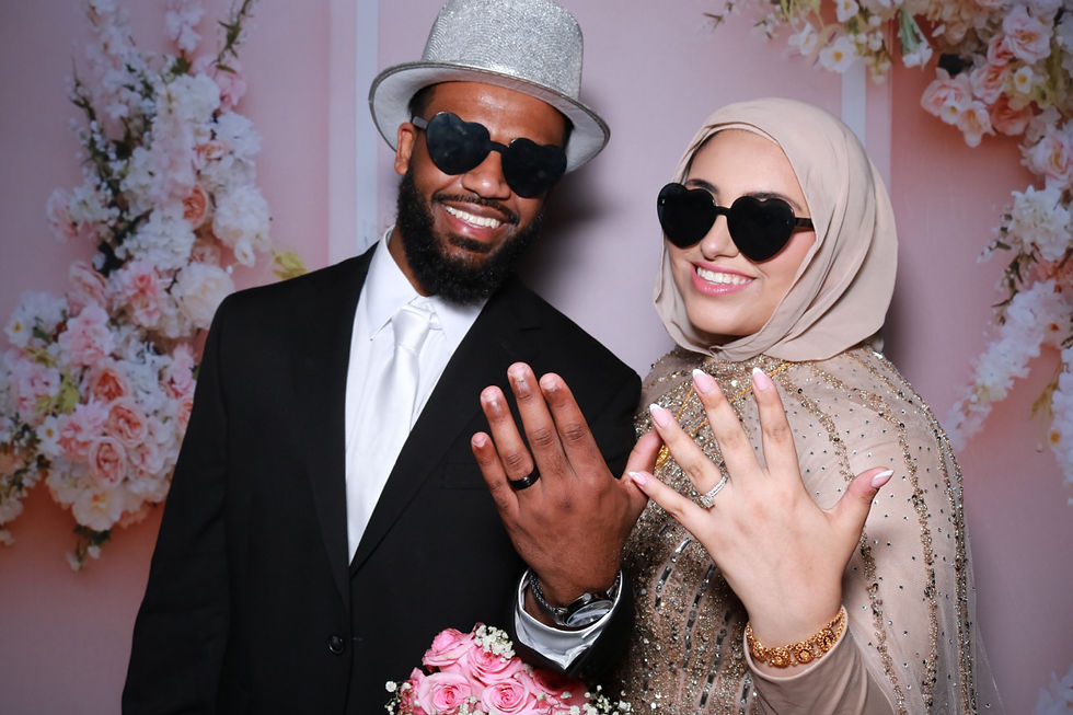 Wedding Photo Booth rental with a floral backdrop as the couple shows their rings in a fun photo.