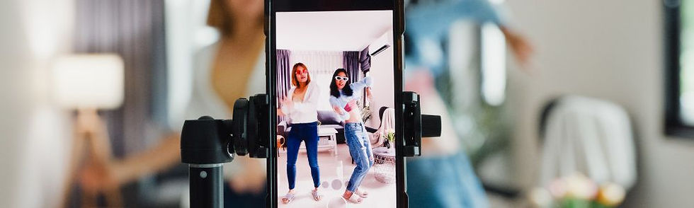 Phone on tripod displays two female content creators dancing in a bright room with a lamp and curtains. The scene captures a lively, joyful mood.