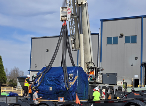 A large crane lifts an oversized load onto a project site.