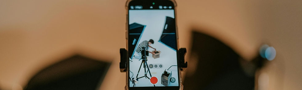 Smartphone on a mount shows a person filming with a tripod in a studio, with blurred lights in the background.