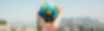 Hand holding a vibrant mini globe against a clear sky and distant mountains, symbolizing exploration and global connection.