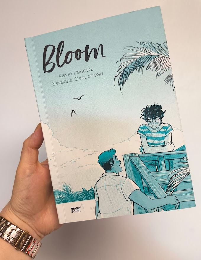 Powieść graficzna pod tytułem Bloom na jasnym tle jest trzymana przez osobę, której rękę widać z boku