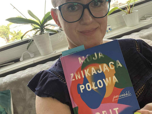 Uśmsiechnięta kobieta w okularach trzyma egzemplarz ksiażki Moja znikająca połowa. W tle okno, parapet z kwiatkiem.