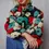 Thumbnail: Front of long-sleeve textured sherpa floral coat with red, teal, white, and black, worn closed with jeans.