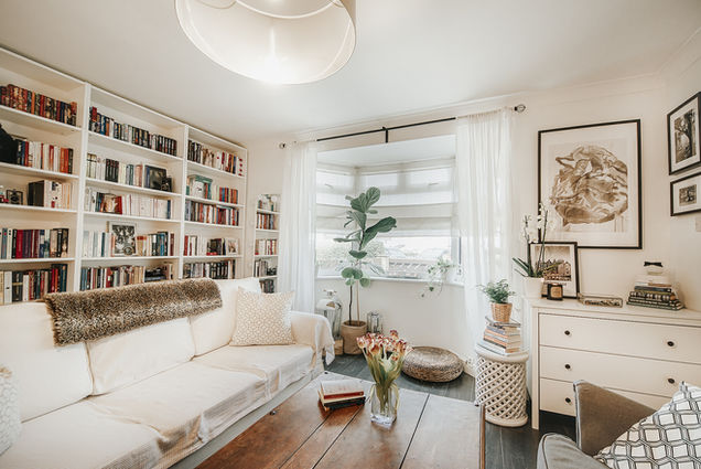 well lit property photo of a living room with a huge bookcase on left and some stylish furniture on right