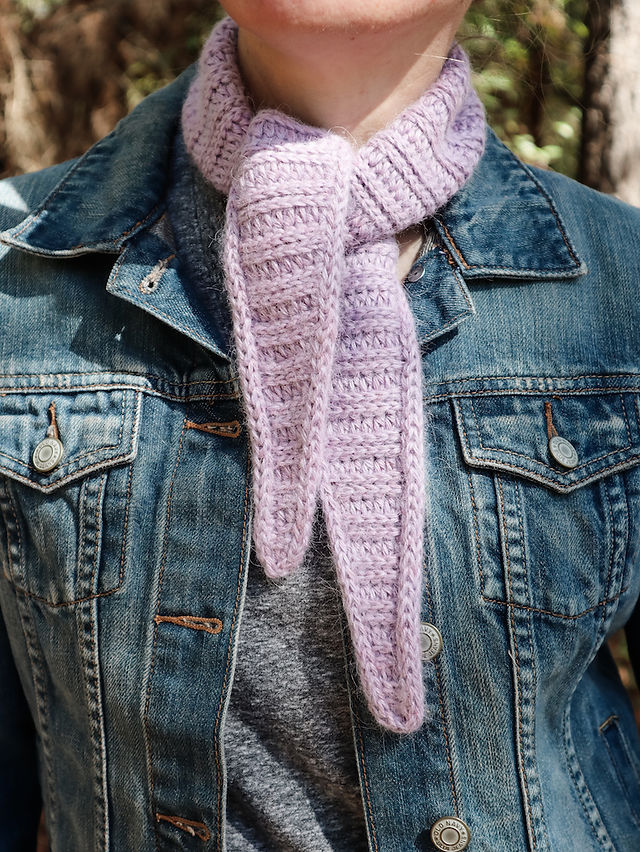girl standing in the woods wearing a handmade mini neck kerchief version of the tapered crochet triangle scarf featuring a ribbed texture hemmed in by an i-cord border