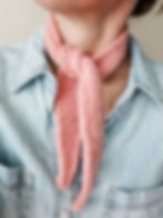 girl wearing a chambray blue shirt modeling a handmade crochet miniature petal pink scarf kerchief tied around her neck