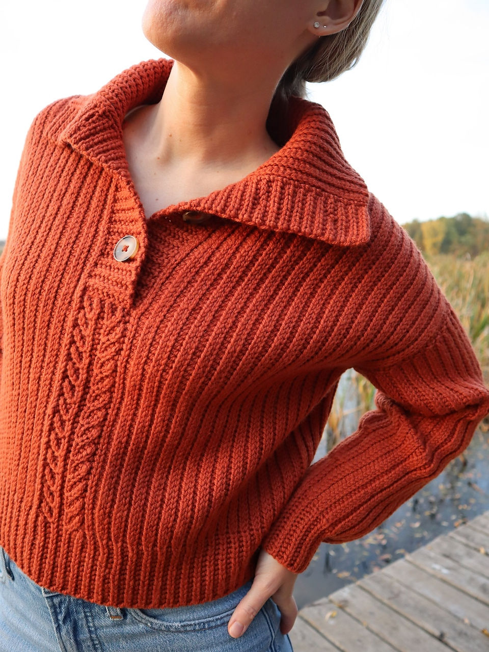 girl modeling handmade crochet sweater featuring a vertical rib texture, cable decorative short row stitches, and half button up closure in a warm autumn orange color