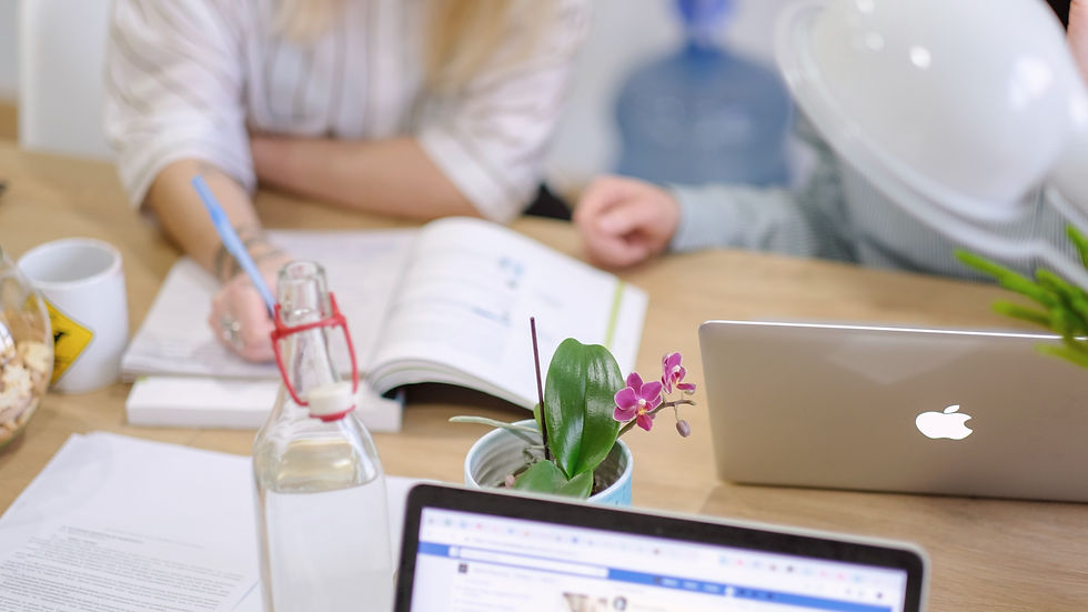 a mother and child work together on back to school homework at wooden desk topped with laptop computers, flowers, water, and books