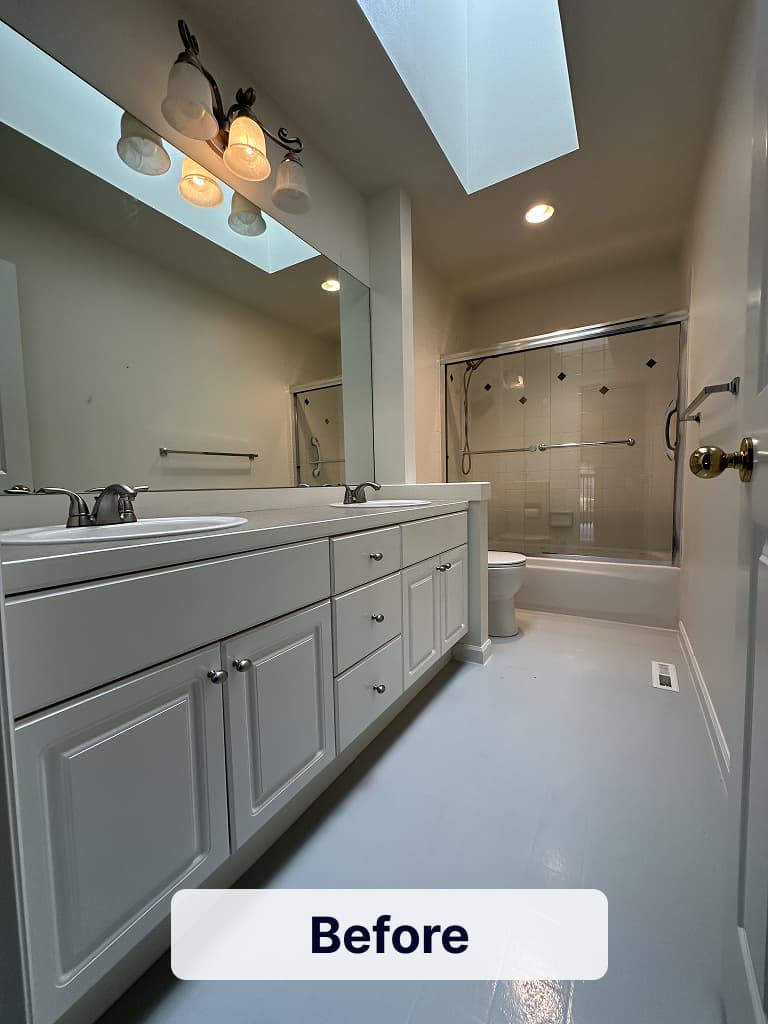 Original bathroom before remodeling with a double vanity, bathtub with shower, skylight, and neutral finishes.