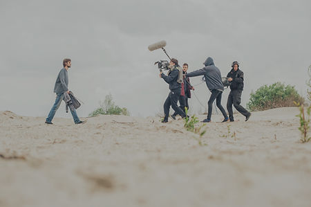 Advertisment being filmed on a beach. A crew with camera and boom mic focus on a single man.