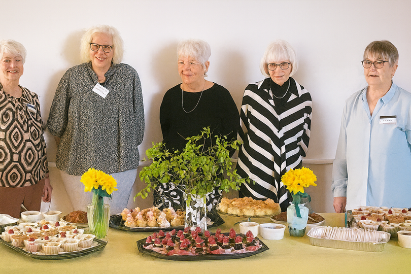 Fem kvinder står bag bord med snacks og kager