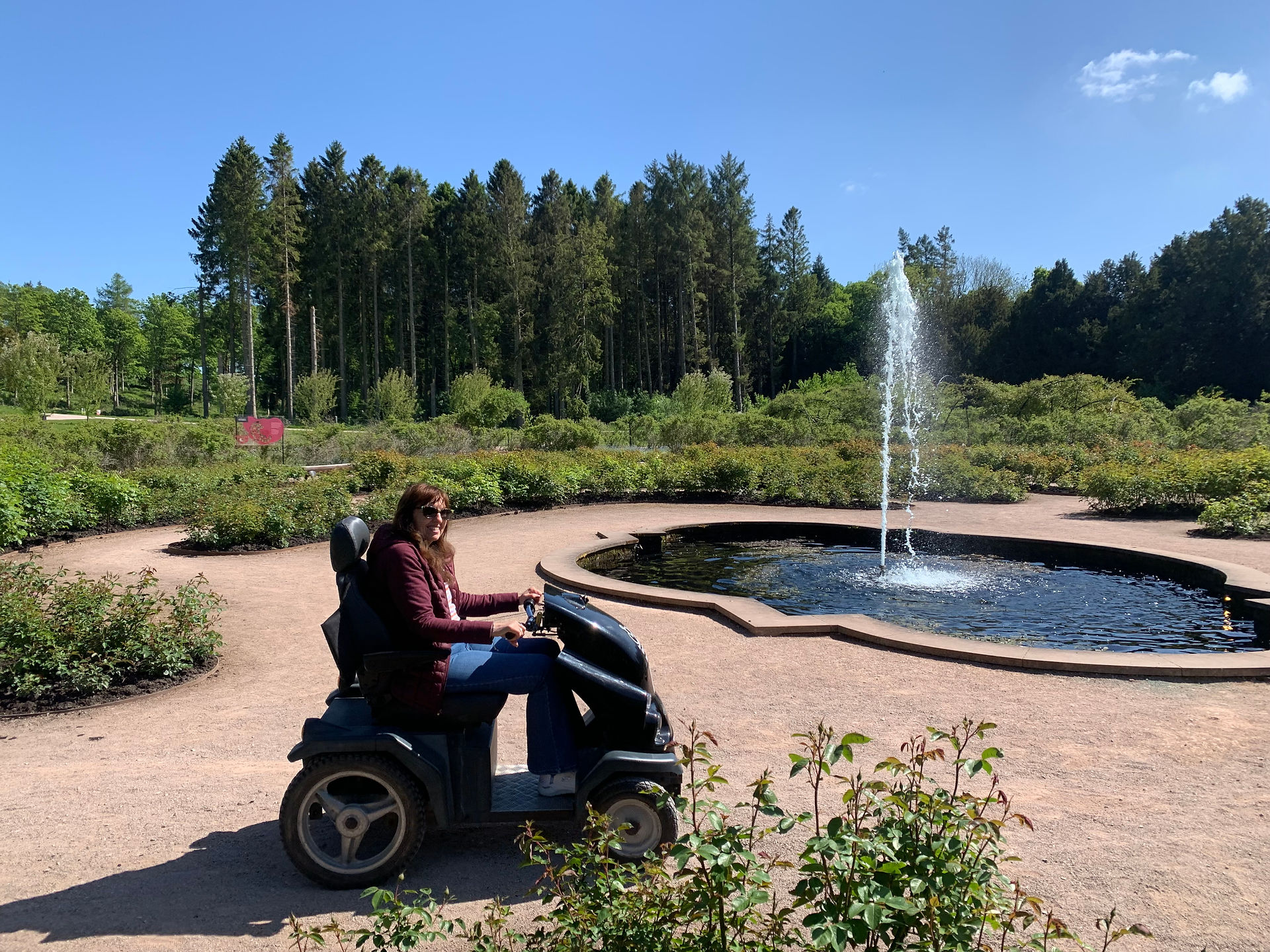 The Tramper at Lowther Castle. The image shows a woman sitting on the Tramper, infront of a fountain. There is lush foliage in the background.