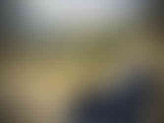 An image of Jane on a Tramper, smiling to the camera. It is a side view image and Jane wears a padded coat and glasses. A glorious mountain view is visible behind her, showing the mountains coming into a valley. The foliage and grass are yellow/green. The sky is cloudy overhead.