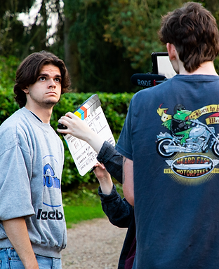 An actor looks at the director of photography who has a clapperboard in his hands. They are engaged in conversation.