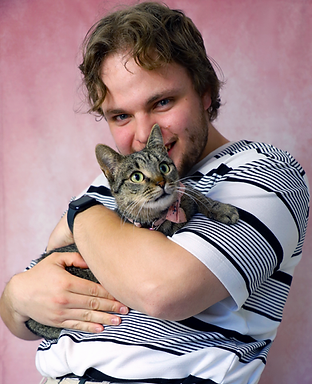 A man with blonde hair and blue eyes cradles Sophie's cat, Flo. The man is wearing a stripy top and is smiling. 