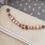 Thumbnail: Taupe wagenspanner met beukenhouten letterkralen op beige achtergrond..