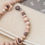 Thumbnail: Taupe wagenspanner met beukenhouten letterkralen en houten bloem.