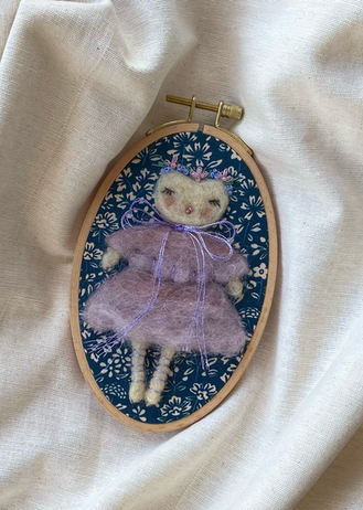 Handgemaakt naaldvilt kunstwerk: roze Lady-Owl met bloemenkroontje op blauwe stof in een ovaal houten borduurraam, op lichte achtergrond.