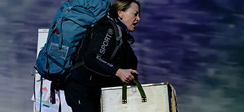 A woman with a backpack and a black trekking jacket walks from left to right