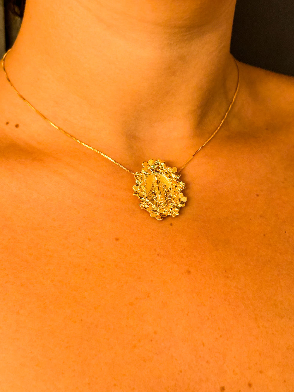 Colar em ouro 18k com a medalha de Nossa Senhora envolta por flores sendo usado por modelo, recorte do colo
