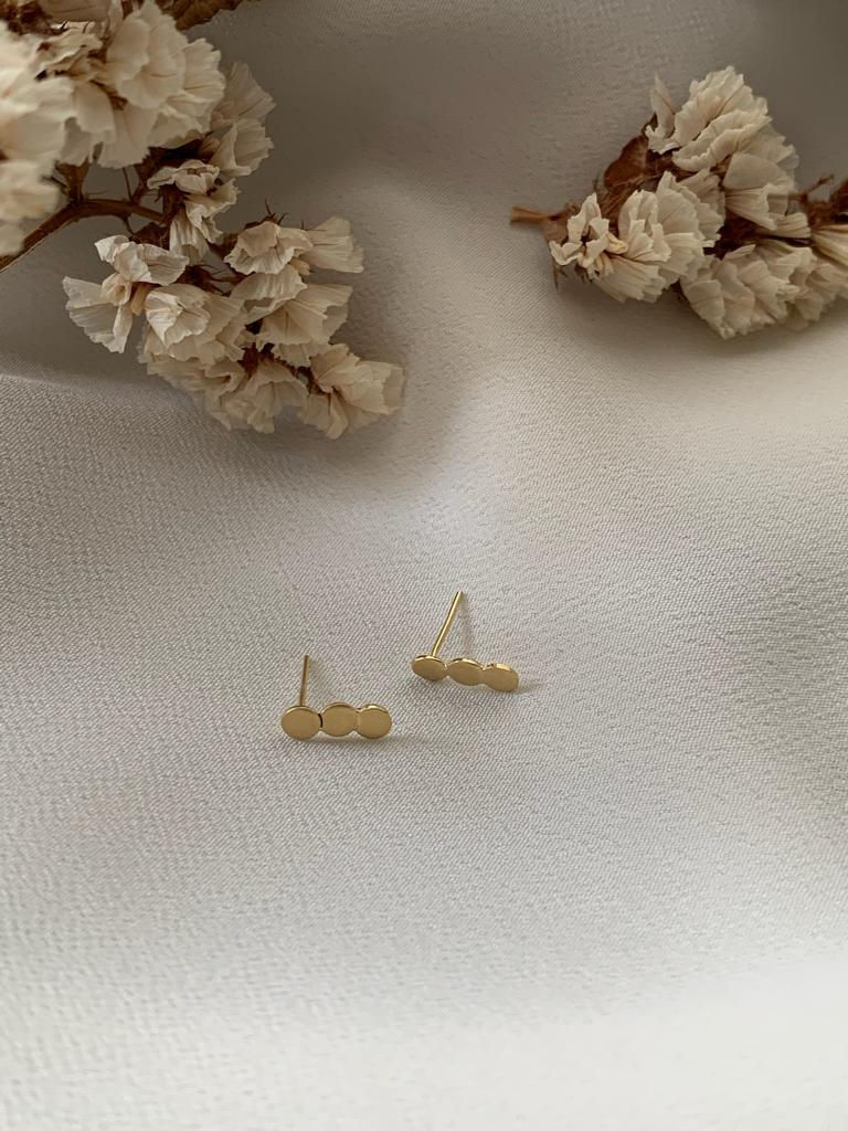 Brinco Amor Infinito em ouro 18k, coleção Mãe de Ouro, ao lado de ramos de flores brancas sobre tecido diáfano branco