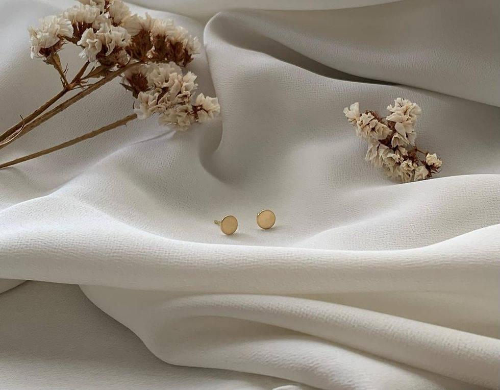 par de Brincos Disco em ouro 18k ao lado de ramo de flores sobre tecido diáfano branco