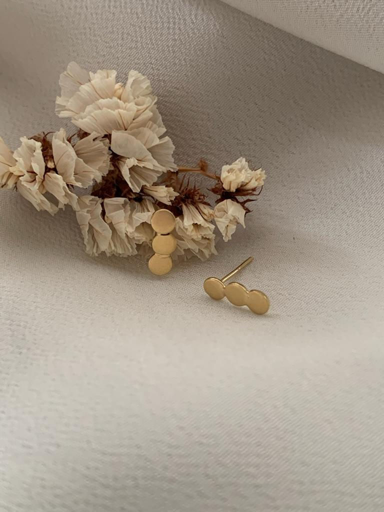 Brinco Amor Infinito em ouro 18k, coleção Mãe de Ouro, ao lado de ramos de flores brancas sobre tecido diáfano branco