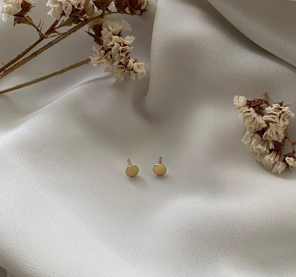 par de Brincos Disco em ouro 18k ao lado de ramo de flores sobre tecido diáfano branco
