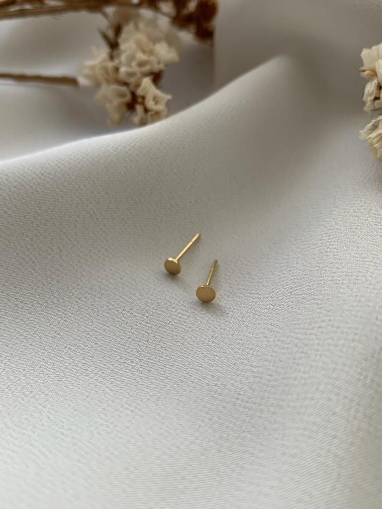 Brinco Célula em ouro 18k cercado por flores brancas sobre tecido diáfano branco