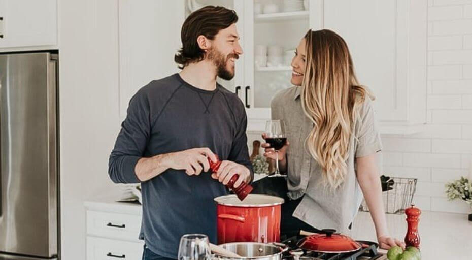 Casal sorrindo na cozinha preparando uma refeição juntos em clima de Dia dos Namorados