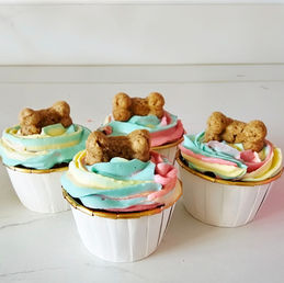 Four colorful cupcakes topped with dog biscuits on a white background. L&V's Bark 'n Bake