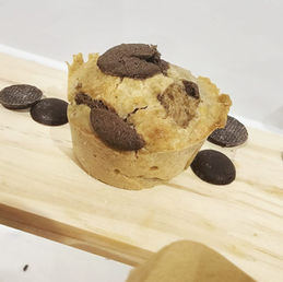Chocolate chip muffin on a wooden surface with scattered chocolates