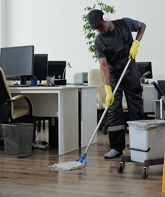 Contemporary young black man workwear cleaning floor open space office