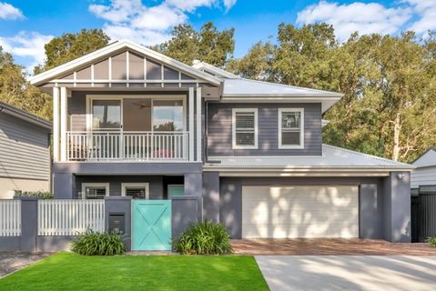 Modern grey house with white balcony, garage, and turquoise gate.