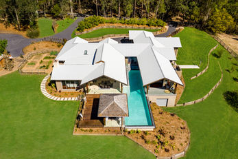 Modern house with pool, large lawn, and surrounding trees.