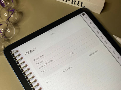 Tablet displaying a project planner with tabs labeled Jan-Dec. Nearby, blocks show "MARCH APRIL" and purple sand timers are visible.
