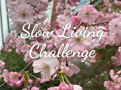 Pink cherry blossoms with "Slow Living Challenge" text overlay. Background shows green leaves, creating a serene and calm mood.