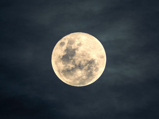 Full moon glowing in a dimly lit cloudy night sky, creating a serene and calm atmosphere.